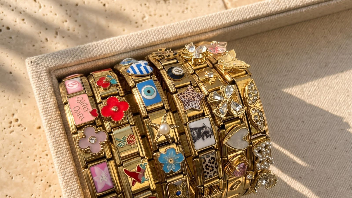 Six bracelets italiens dorés composés de charms émaillés, posés sur un plateau en lin
